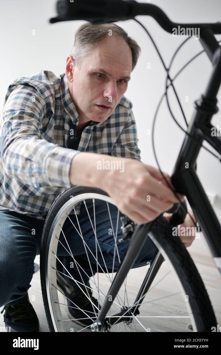Reifer Kaukasischer Mann stellt die Bremse seines neuen Fahrrads ein In Innenräumen Stockfoto