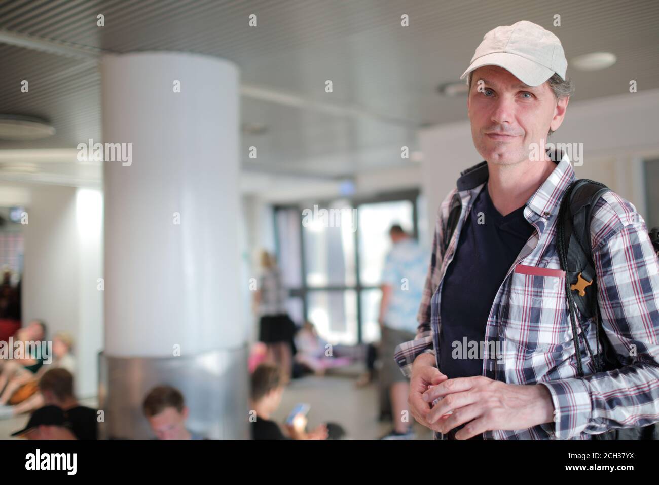 Kaukasischer Mann mit Rucksack, der in einer überfüllten Wartehalle steht Eines Passagierterminals und Blick auf die Kamera Stockfoto