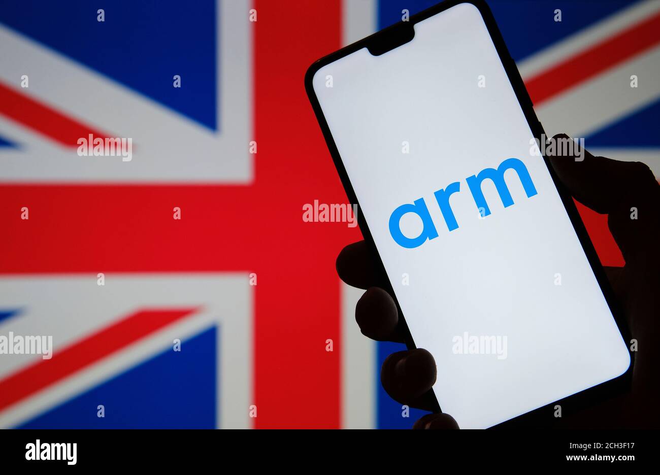 ARM Holdings Logo auf der Silhouette des Smartphone halten gesehen In der Hand und das Vereinigte Königreich Flagge auf einem verschwommen Hintergrund Stockfoto