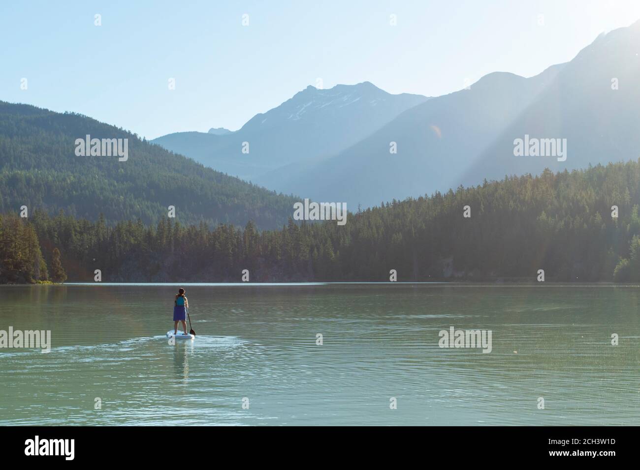 Rückansicht von anonymen Frauen, die an sonnigen Tagen im Hochland von British Columbia, Kanada, auf einem ruhigen See in der Nähe von Bergen und Wäldern reiten Stockfoto