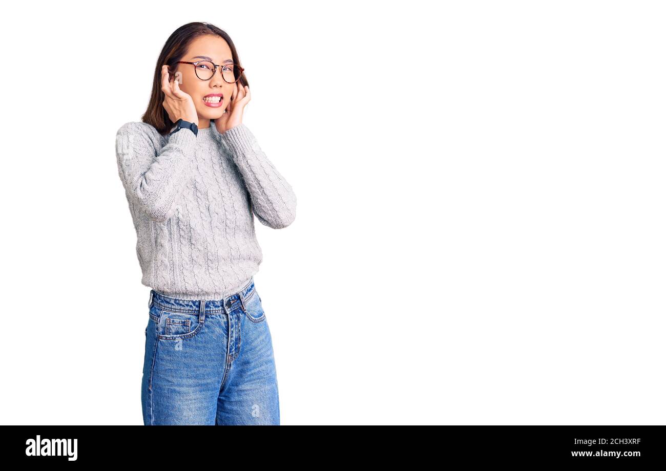 Junge schöne chinesische Mädchen tragen lässige Kleidung, die Ohren mit Fingern mit genervten Ausdruck für den Lärm der lauten Musik. Taub Konzept. Stockfoto