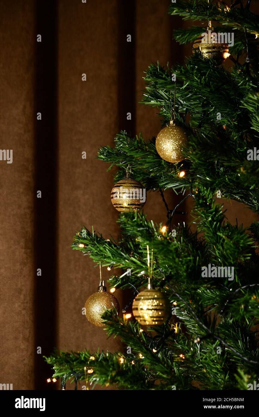 Fragment der Hälfte des Weihnachtsbaums mit goldenen Kugeln und glühender dekorativer Girlande mit gelben Lichtern. Stockfoto