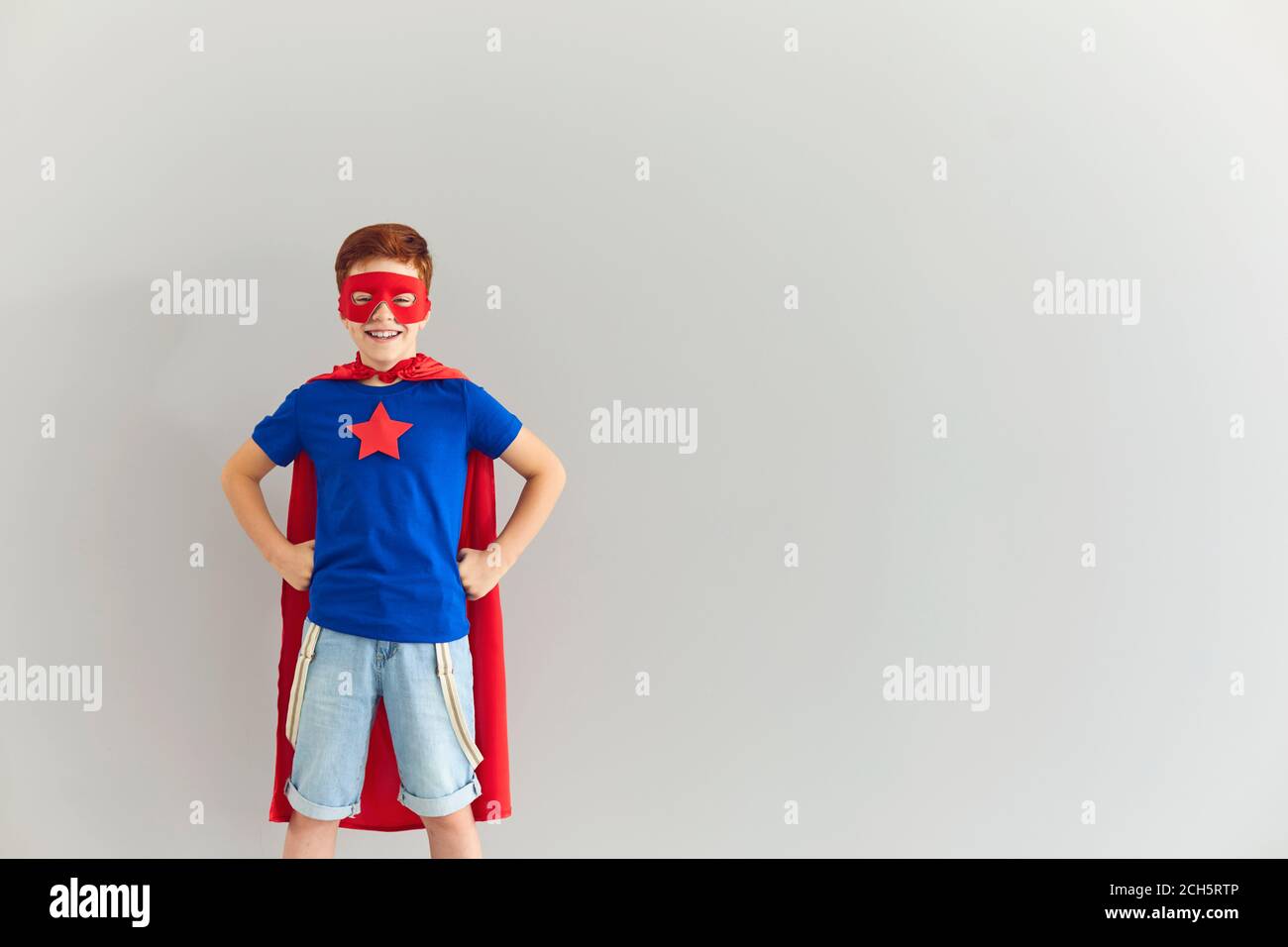 Lächelnder Junge im Kostüm des Superhelden Blick auf Kamera über grauen Hintergrund, kopieren Raum Stockfoto
