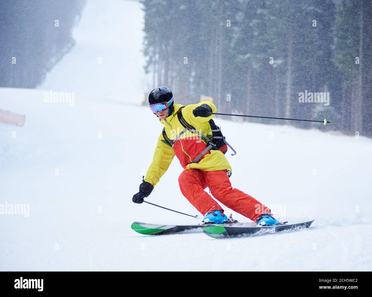 Vorderansicht des jungen männlichen Skifahrers Abfahrtsski und tun Carve Turn auf hohen schneebedeckten Hang. Skifahren bei Schneefall in den Bergen. Einfache Abfahrt. Winter nebligen Hintergrund. Aktives sportliches Lifestyle-Konzept. Stockfoto