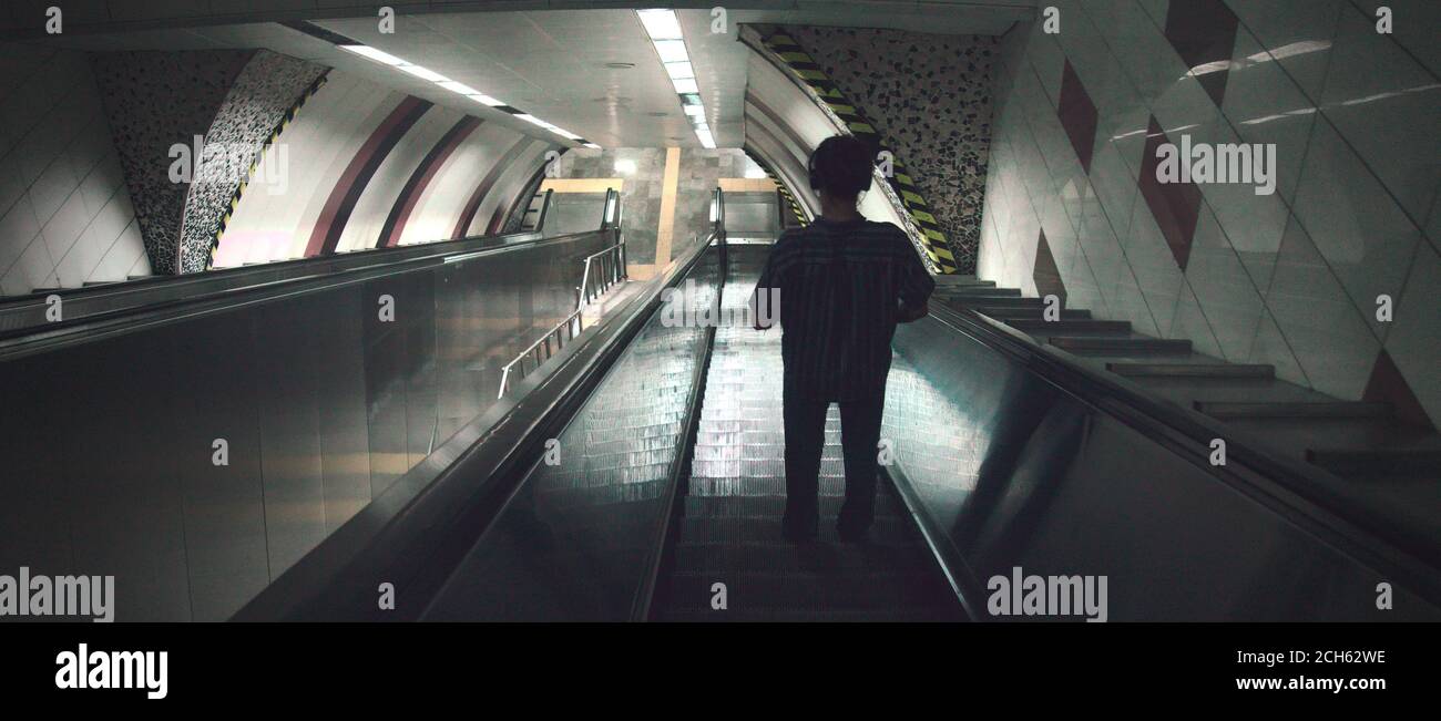 Silhouette des jungen Mannes, der Musik mit Kopfhörer im Stehen hört Auf der Rolltreppe, die in der U-Bahn nach unten geht Stockfoto