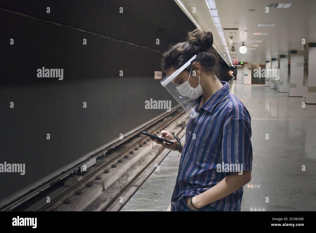 Langhaarige isolierte und intelligente Teenager spielen mit seinem Telefon Während wir auf die U-Bahn warten, die alleine kommt Stockfoto