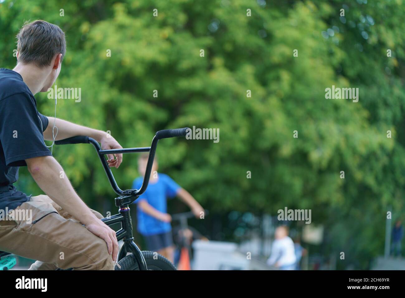 BMX in Moskau öffentlichen Park. Tapferer junger Biker, der sich nach einem Stunt am Sommertag ausruhte. Extremsport ist bei Jugendlichen sehr beliebt. Rückansicht/Rückansicht. Defocuse Stockfoto