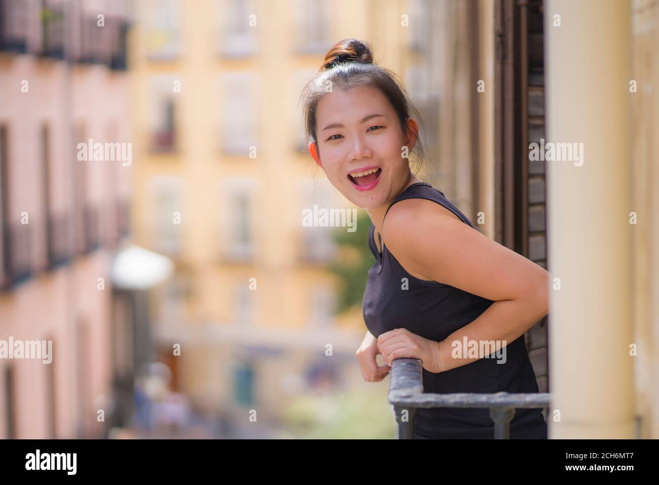 Junge glücklich und schöne asiatische koreanische Frau im Haar bun Genießen Sie den Blick auf die Stadt vom Balkon des Hotelzimmers in Spanien während Urlaub Reise in Europa lächelnd ch Stockfoto