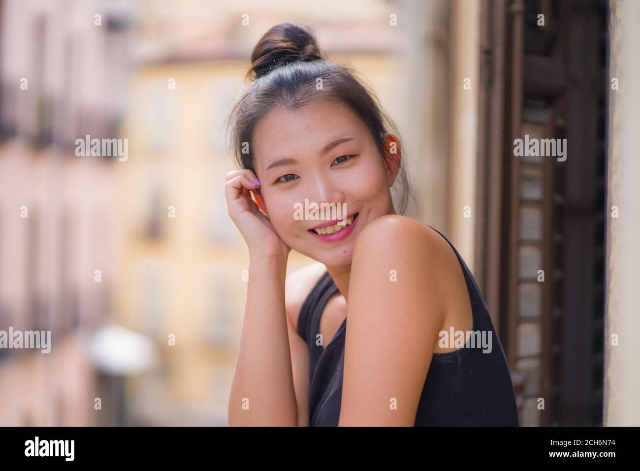 Junge glücklich und schöne asiatische koreanische Frau im Haar bun Genießen Sie den Blick auf die Stadt vom Balkon des Hotelzimmers in Spanien während Urlaub Reise in Europa lächelnd ch Stockfoto