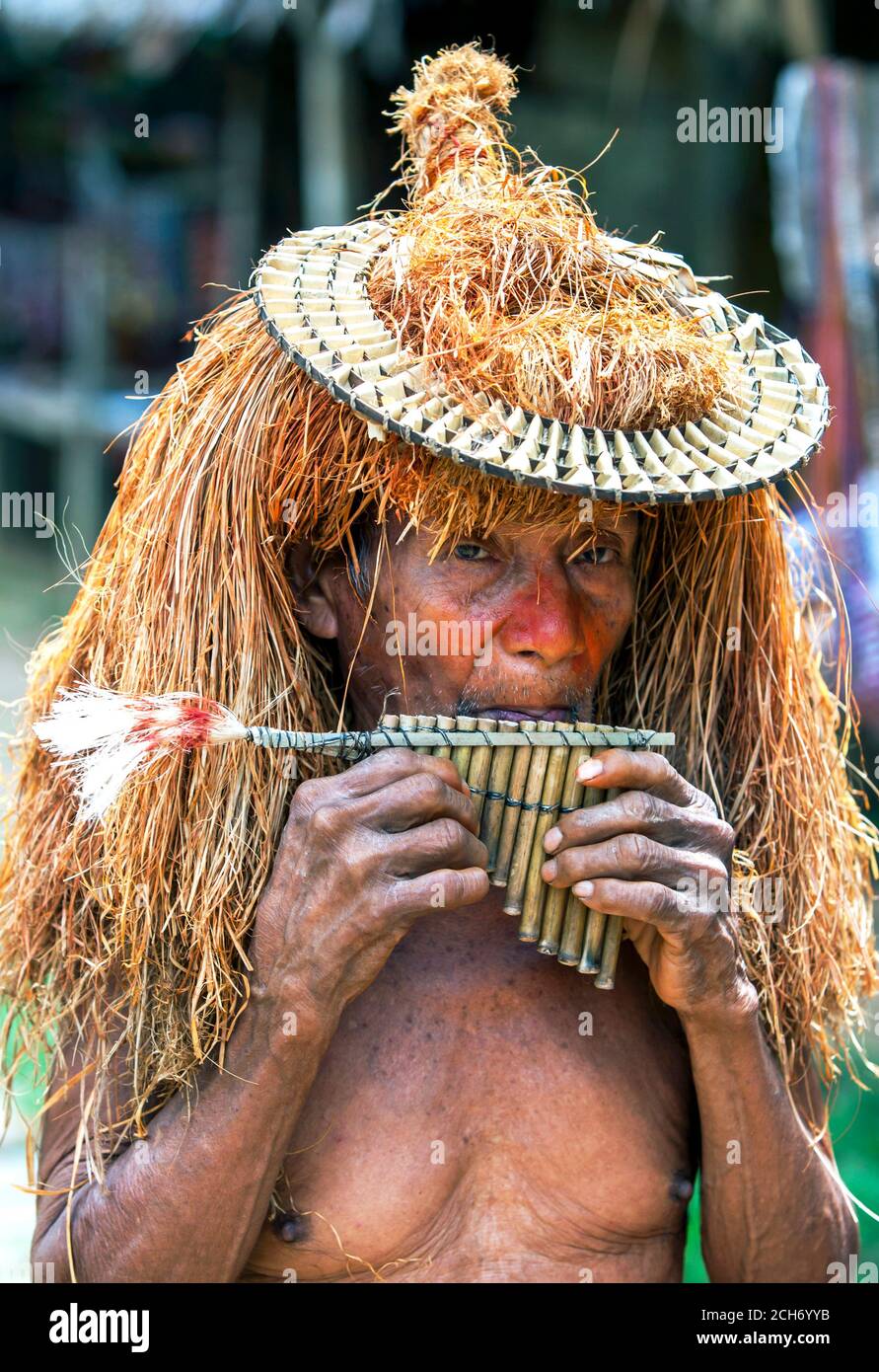 Ein älterer Mann in traditionell indischer Tracht spielt eine handgefertigte Pfeifenflöte in der Nähe von Iquitos am Amazonas in Peru. Stockfoto