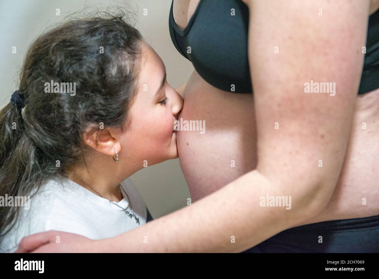 Junges Mädchen küsst den Bauch ihrer schwangeren Mutter. Stockfoto