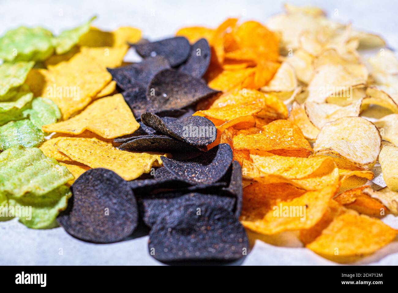 Verschiedene Arten von farbigen Kartoffelchips, grauer Hintergrund. Fast-Food-Konzept, ungesunde fetthaltige Kohlenhydrat-Lebensmittel. Stockfoto