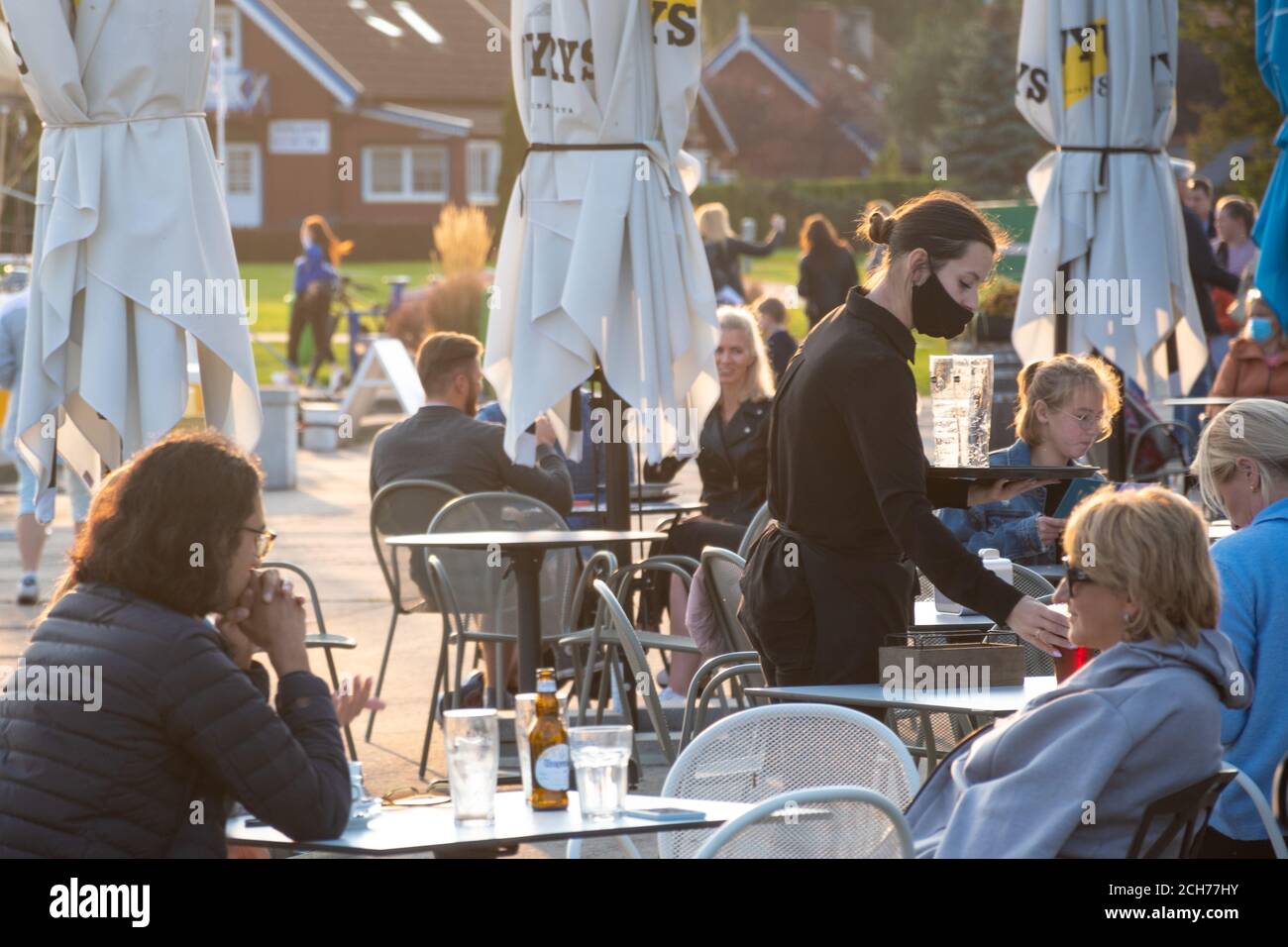 Kellnerinnen mit einem maskierten Serviertisch einer Außenbar, eines Cafés oder Restaurants mit blonden Mädchen am Tisch während der zweiten Welle von Covid oder Coronavirus Stockfoto