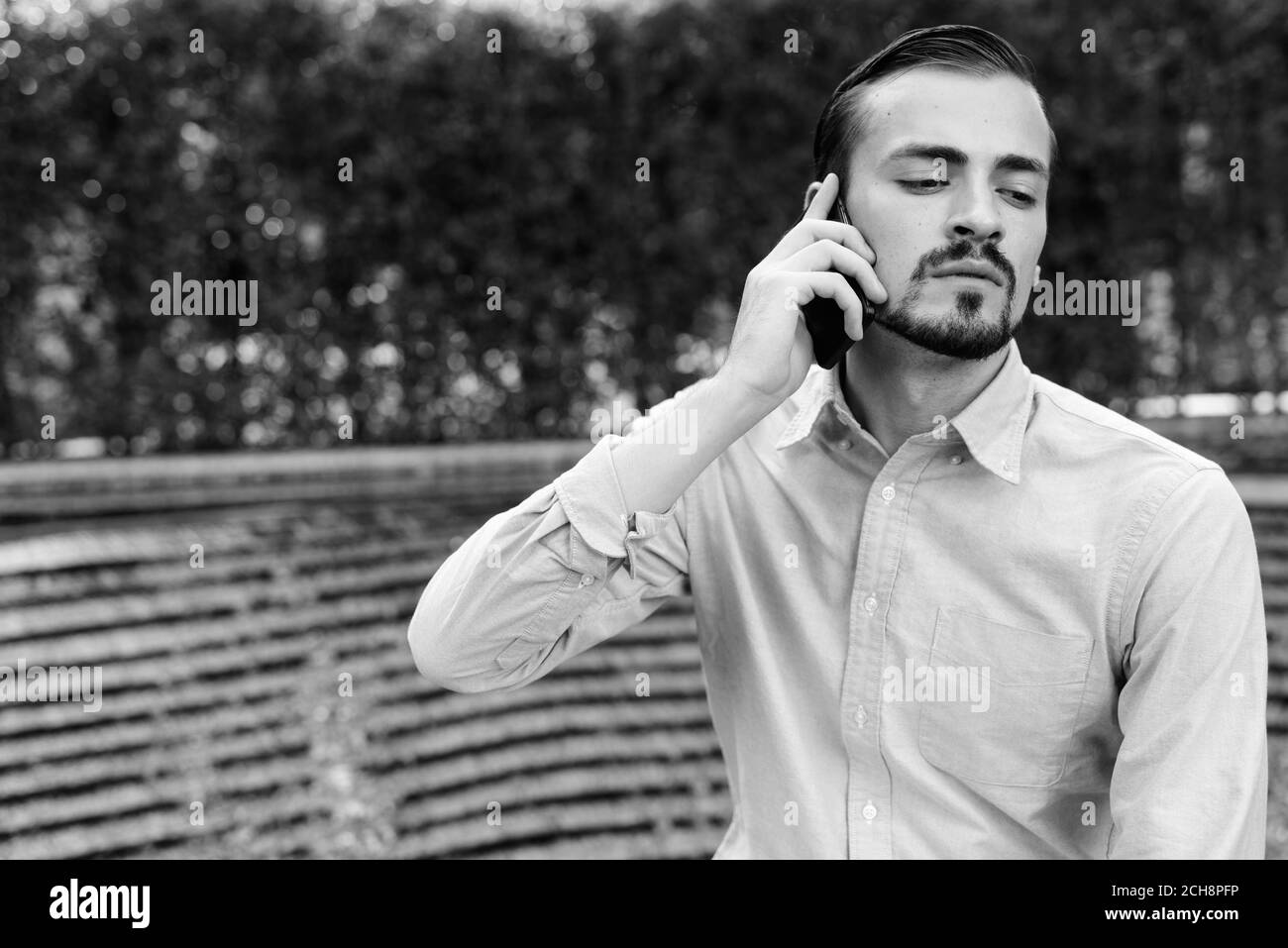 Junge gut aussehende bärtige Geschäftsmann im Gespräch am Telefon in der Stadt im Freien Stockfoto
