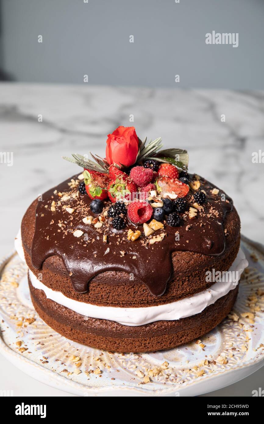 Schokoladenkuchen gefüllt mit Sahne, gekrönt mit Waldbeeren und einer Rose. Stockfoto
