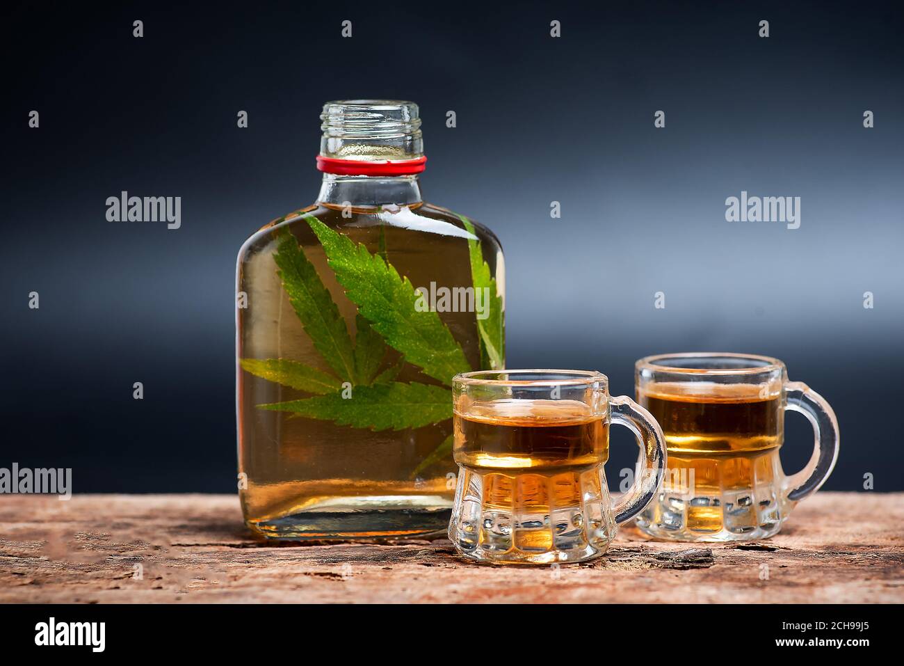 Alkoholisches Getränk wie Whiskey Brandy oder Schnaps mit Cannabis infundiert Blätter in der Flasche auf dem Tisch mit dunkler Kopie Platz Stockfoto