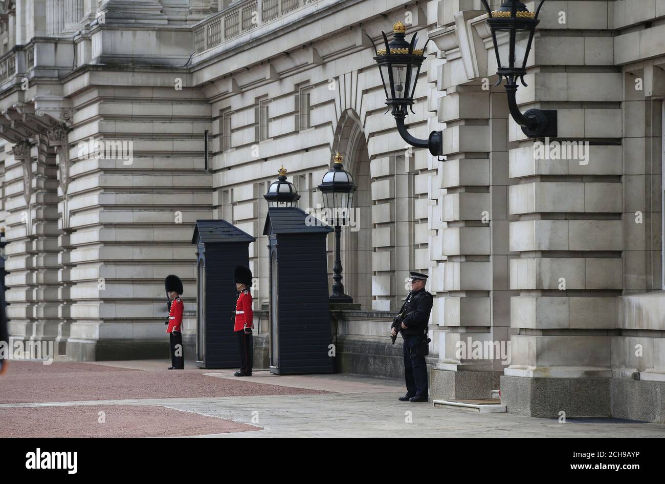 Ein bewaffneter Polizeibeamter und Soldaten der irischen Garde auf dem Vorplatz des Buckingham Palace im Zentrum von London. Scotland Yard hat gesagt, dass ein 41-jähriger Mann festgenommen wurde, nachdem er am Mittwochabend eine Umfassungsmauer am Palast bestochen hatte. Stockfoto