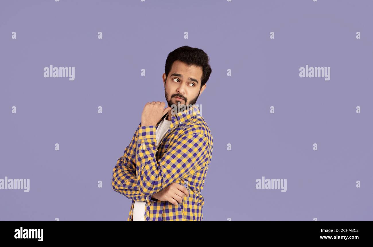 Nachdenklicher indischer Kerl, der über seine Schulter auf leeren Raum schaut, flieder Hintergrund Stockfoto