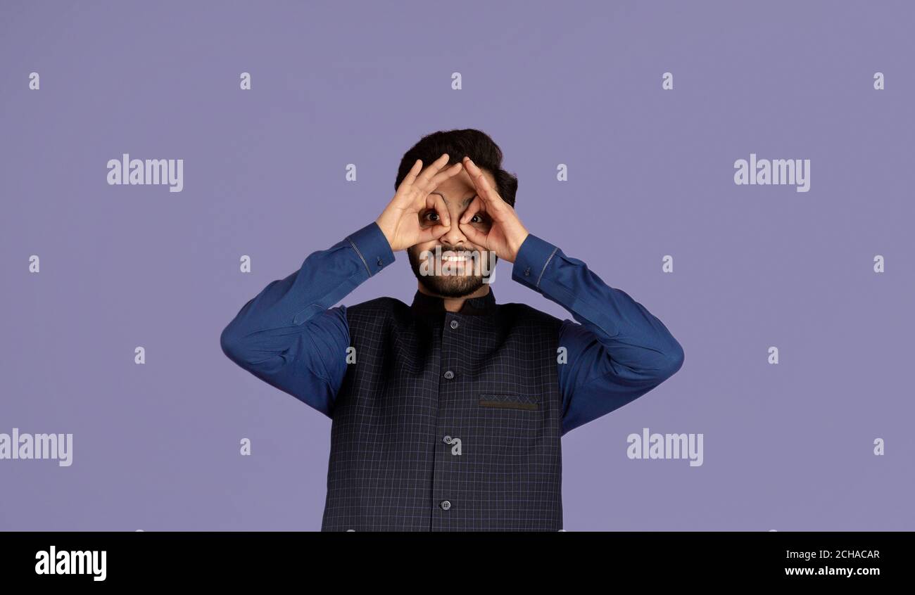 Porträt eines Comic-Indianers, der die Finger wie eine Brille an die Augen hält, violetter Hintergrund Stockfoto