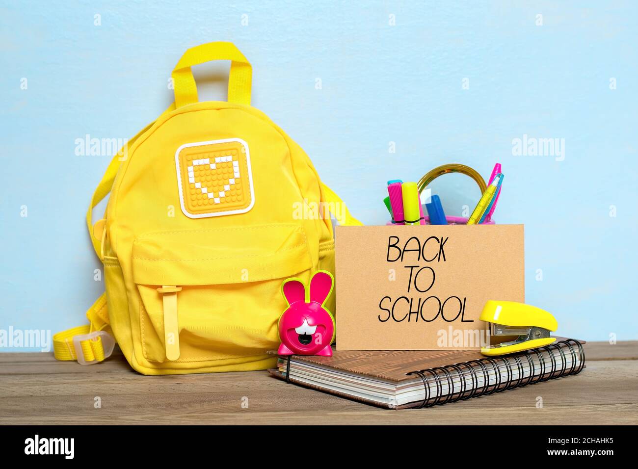 Zurück zur Schulkomposition, Bildungskonzept. Gelber Rucksack mit Schulbedarf - Notizbuch, Stifte, Hefter, Bleistift, Spitzer isoliert auf blau Stockfoto