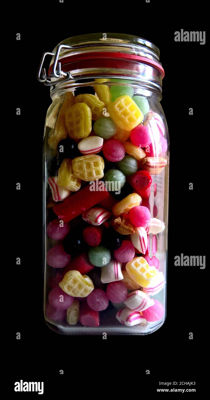 Glas gefüllt mit verschiedenen Bonbons auf schwarzem Hintergrund Stockfoto