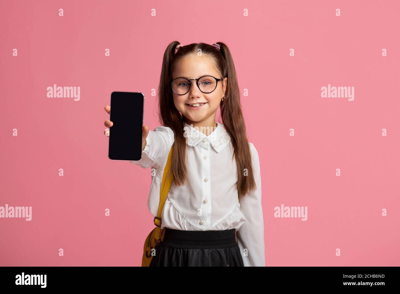 Technologie und Schule. Kleines Kind in Brille in Uniform zeigt Telefon Stockfoto