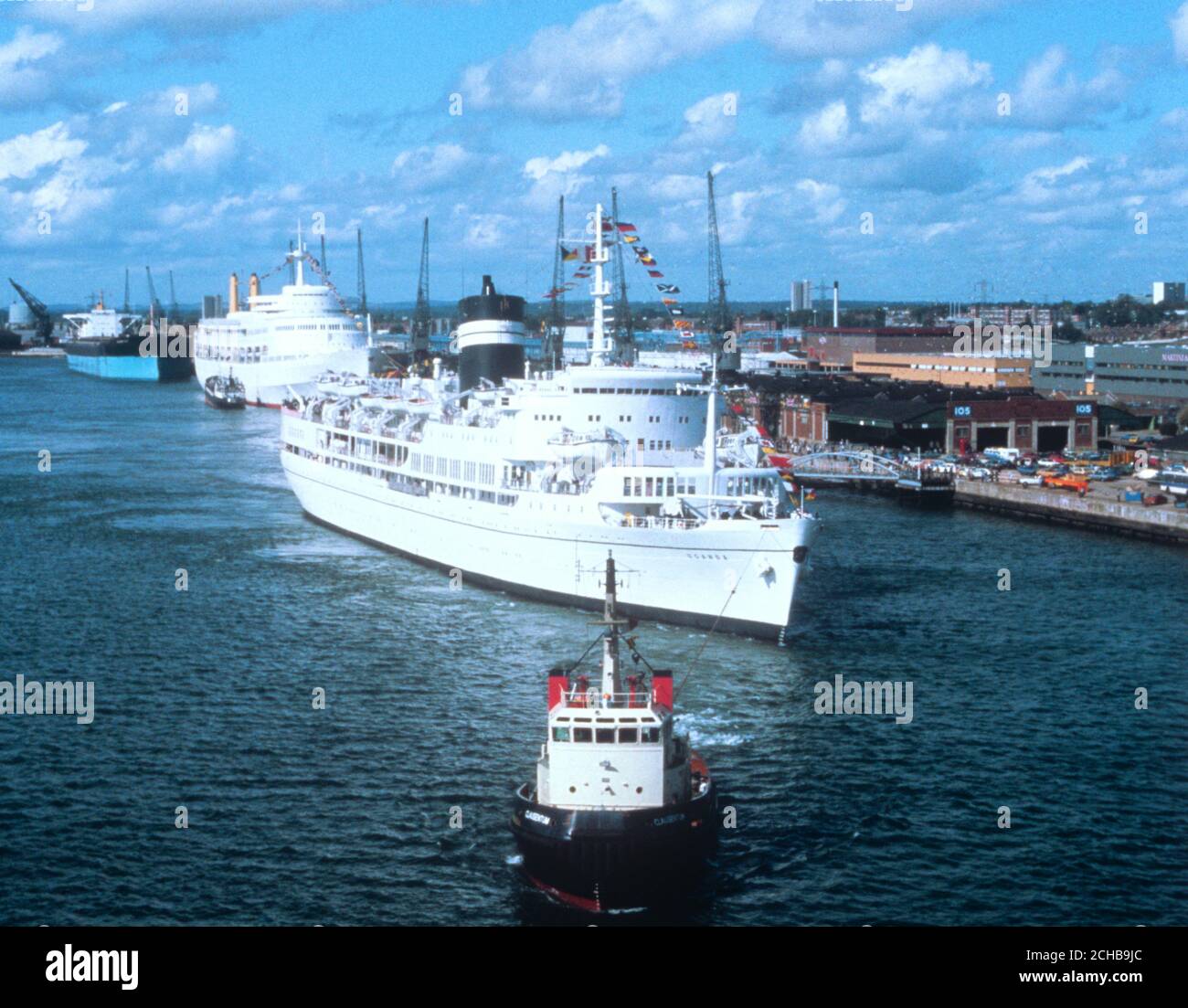 Die SS Uganda, die mit Ammergeflechtungen bejagt ist, wird von ihrem Anlegeplatz am Kai in Southampton weggezerrt. Das BI Discovery Kreuzfahrtschiff, die SS Uganda, wurde während des Südatlantikkonflikts an die Falklands Task Force als Spitalschiff requiriert. Heute ging das 17,000 Tonnen schwere Schiff wieder in den Passagierdienst und verließ Southampton für eine Mittelmeerkreuzfahrt. Stockfoto