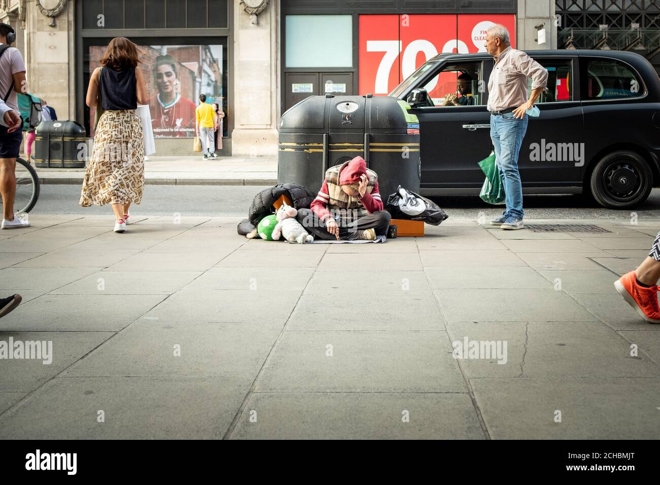 London - September 2020: Ein Obdachloser sitzt versumpt, während die Käufer an der Oxford Street vorbei laufen Stockfoto