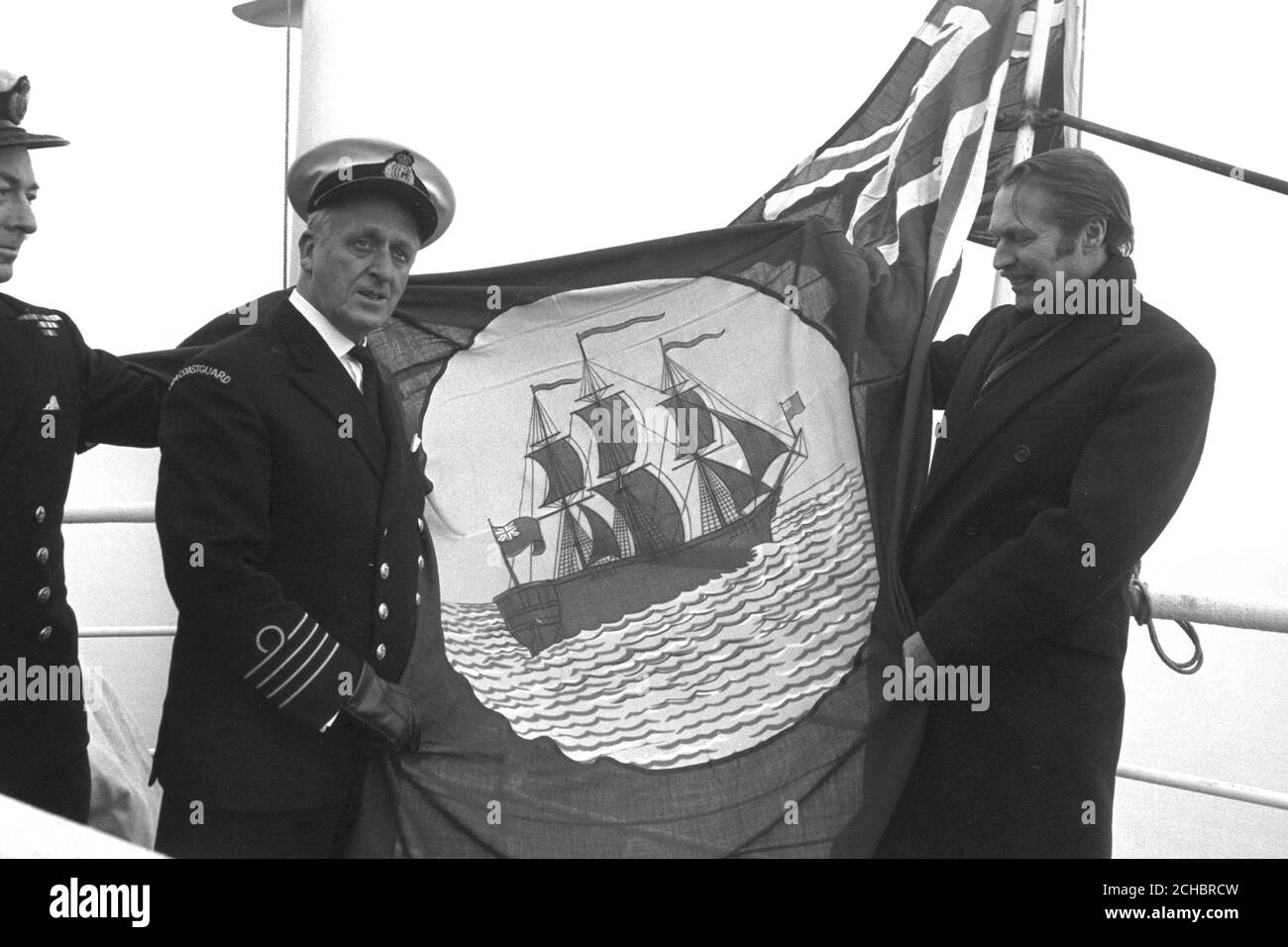 Anthony Grant (rechts), Parlamentarischer Staatssekretär für Handel und Industrie, beim "Brechen der Flagge" auf der 1,500 Tonnen schweren Miranda, die speziell als Mutterschiff und Krankenhausschiff für die Fischereiflotte vor Island umgebaut wurde. Auf der linken Seite ist ihr Kommandant, Kapitän RKN Emden. Stockfoto