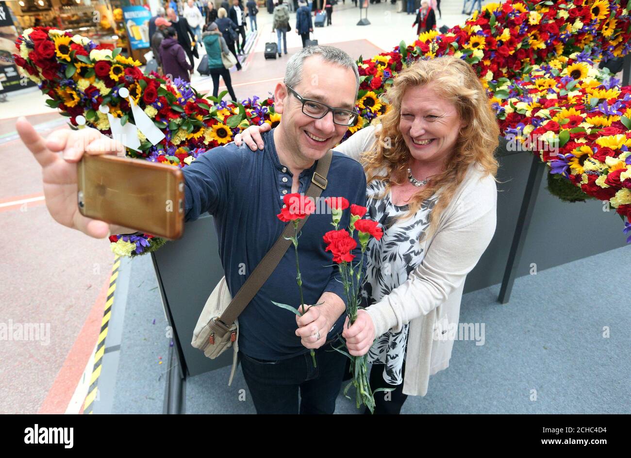 Der Fernsehgärtner Charlie Dimmock lässt sich mit einem Pendler ein Selfie machen, während er am Londoner Bahnhof Victoria ein Blumenflugzeug enthüllte, das aus 10,000 Blumen besteht, die von der Billigfluggesellschaft und dem neuen Monarch-Reiseziel stammen. Stockfoto