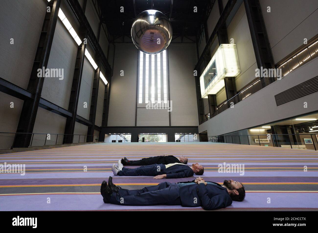 Das dänische Kollektiv SUPERFLEX liegt unter einem riesigen Pendel, Teil ihrer interaktiven Großinstallation One Two Three Swing!, während der Enthüllung der Tate Modern Hyundai Commission 2017 in der Tate Modern im Zentrum von London. Stockfoto