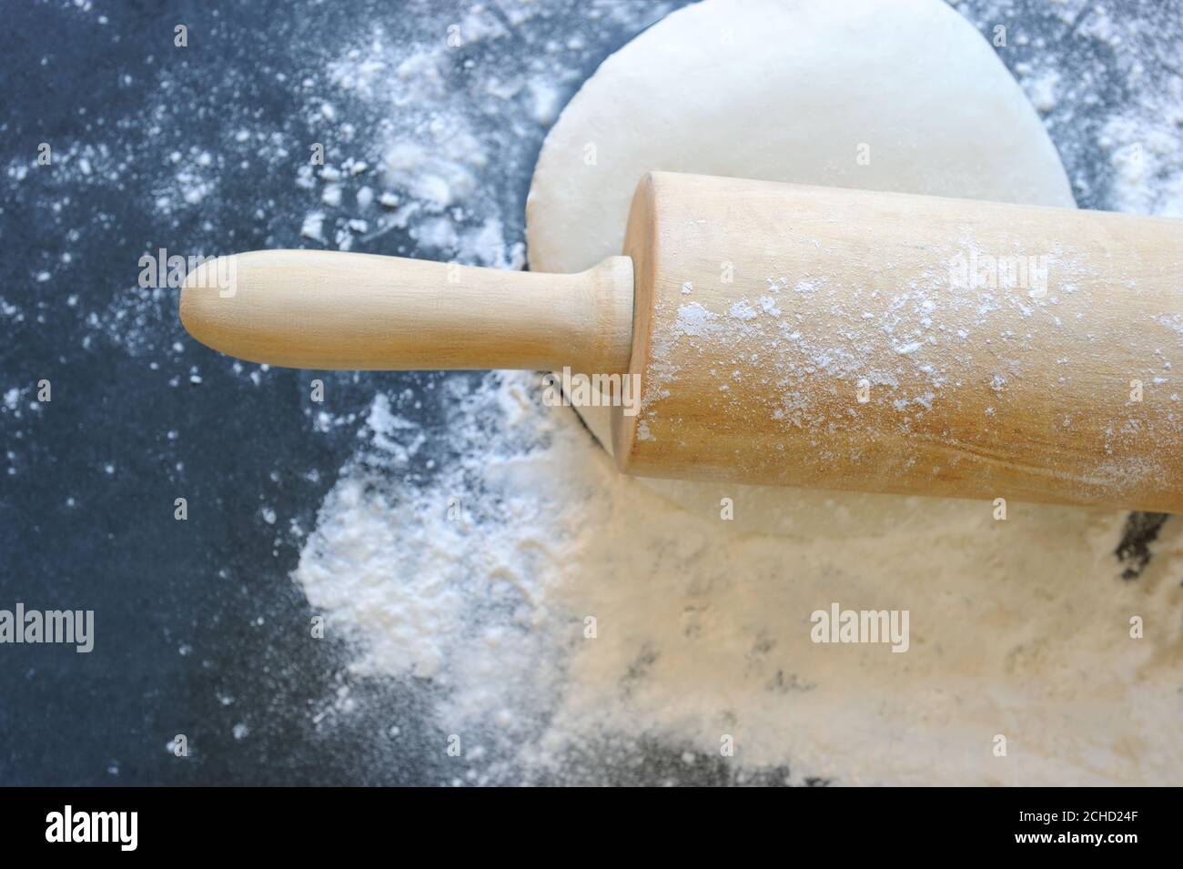 Nudelholz mit Teig und Mehl auf dem dunklen Hintergrund. Selektiver Fokus. Horizontal mit Platz für Text. Stockfoto