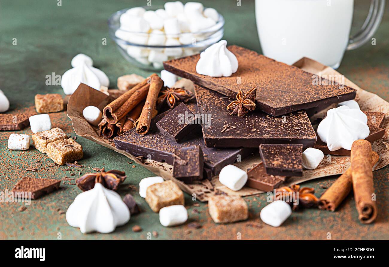Zutaten für die Herstellung von heißer Schokolade. Dunkle und Milchschokolade, Kakaopulver, Zimt, Anis-Stern, brauner Zucker, Marshmallow, Baiser und Milch über gr Stockfoto