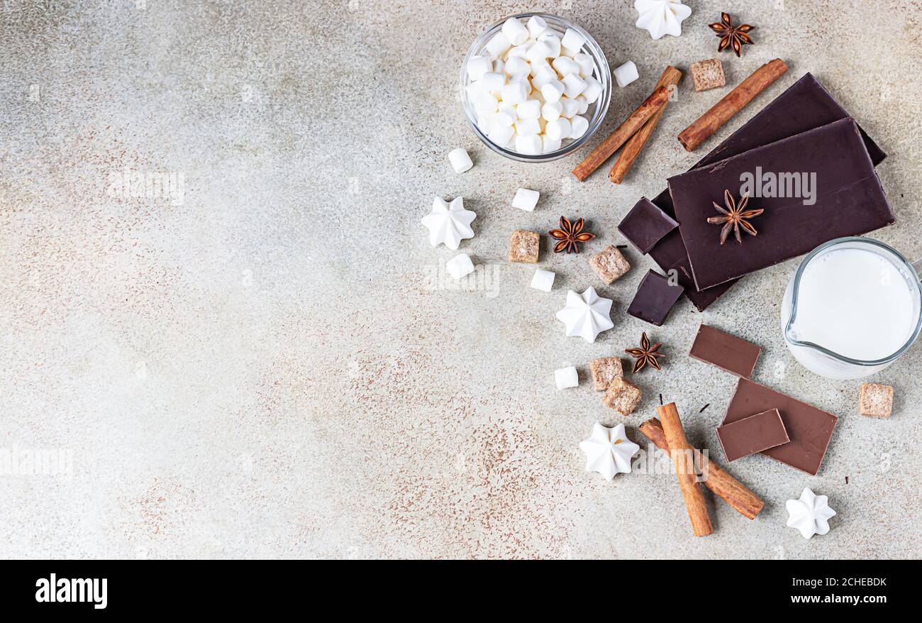 Dunkle und milchige Schokolade, Zimt, Anisstern, brauner Zucker, Marshmallow, Baiser und Milch auf hellem Hintergrund. Zutaten für die Herstellung von heißer Schokolade Stockfoto