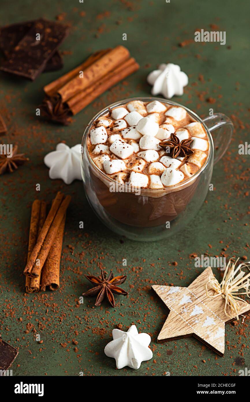 Glas Tasse heiße Schokolade oder Kakao mit Marshmallows und Anis Stern, Stücke von Schokolade, Meringue und Gewürze auf grünem Hintergrund. Traditioneller Winter Stockfoto