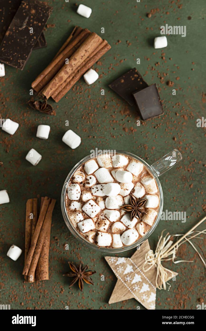 Heißer Kakao oder Schokolade mit Marshmallow, Anisstern, Zimt und Schokoladenstücken. Selektiver Fokus, grüner Stein Hintergrund. Gemütliches Urlaubskonzept, Stockfoto
