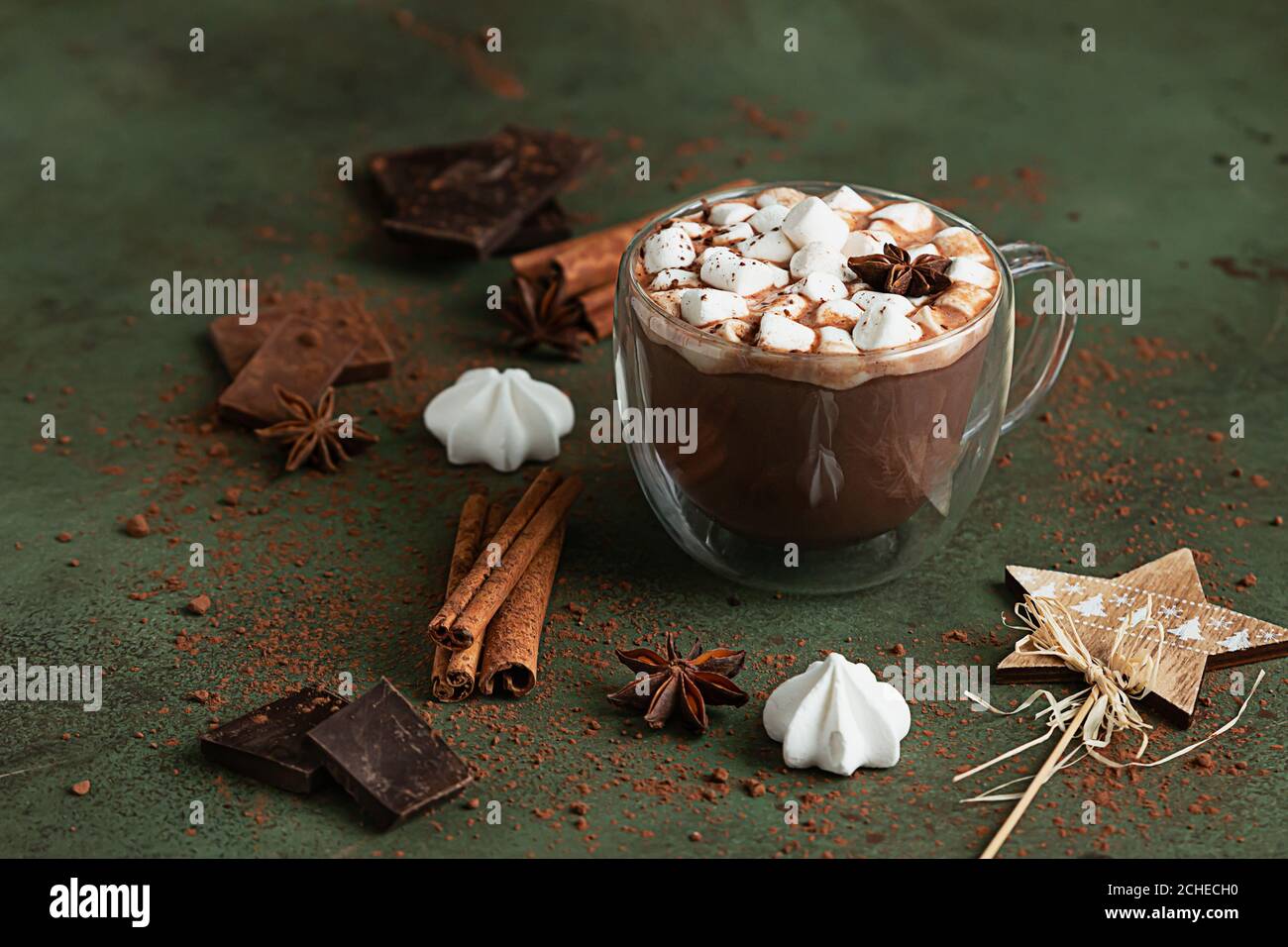 Glas Tasse heiße Schokolade oder Kakao mit Marshmallows und Anis Stern, Stücke von Schokolade, Meringue und Gewürze auf grünem Hintergrund. Traditioneller Winter Stockfoto
