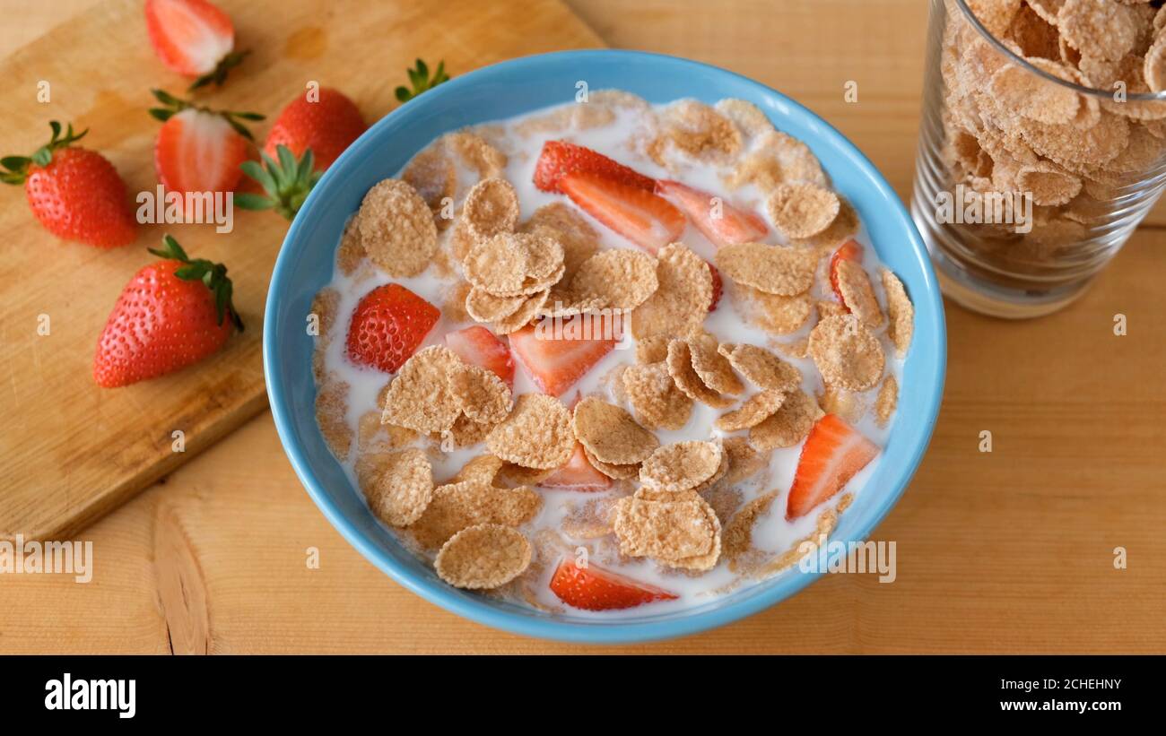 Vollkornflocken mit Milch und Erdbeeren in blauer Schale auf Holztisch. Gesundes Frühstück Stockfoto