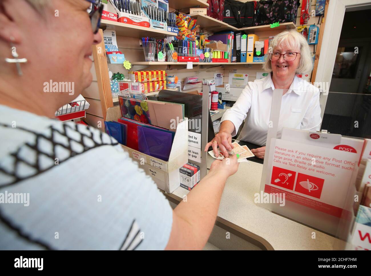 Ein Kunde zieht Bargeld von der Post Office Managerin Carol Starkey bei der Post in Wells Next the Sea, Norfolk, ab, wie Untersuchungen der Post ergeben haben, dass viele Banken kleine Stadtfilialen schließen, Diejenigen, die sich für einen Aufenthalt in Großbritannien entscheiden, haben Schwierigkeiten, eine Bank oder einen Geldautomaten zu finden, um im Urlaub Bargeld abzuheben. Stockfoto