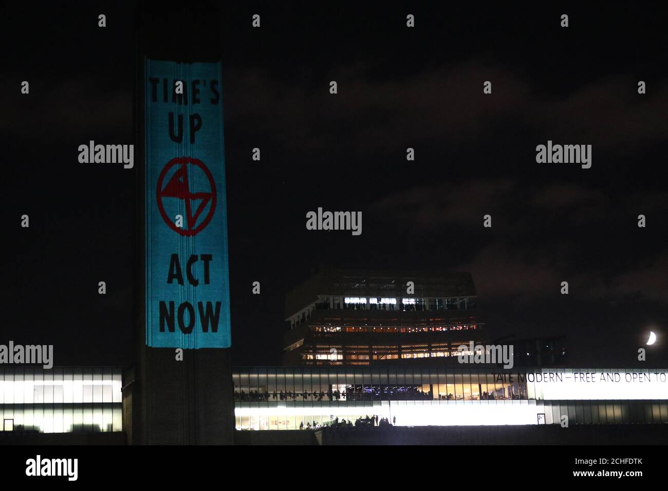 Extinction Rebellion-Aktivisten gehen durch die Tate Modern, während andere Botschaften auf das Gebäude in London projizieren. Die Gruppe kündigte diese Woche an, dass sie in den nächsten zwei Wochen auf die Straße gehen werde, plante, Straßen um Westminster zu schließen und im Rahmen ihrer Proteste einen Sit-in am Londoner City Airport zu veranstalten. Stockfoto