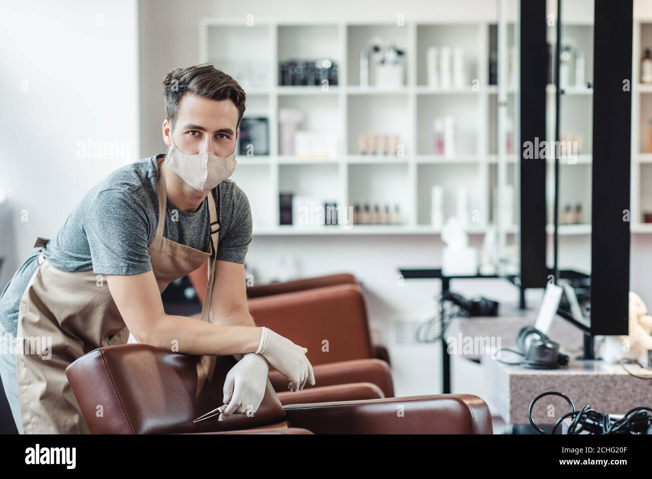 Männlicher Friseur in Schutzmaske und Handschuhe warten auf Kunden Im leeren Salon Stockfoto