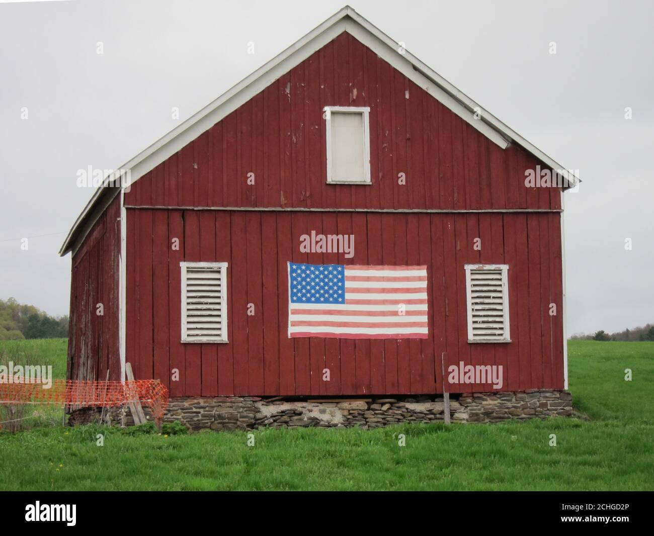 Klassische rote Holzscheune mit großer amerikanischer Flagge Die Seite in einer ländlichen Landschaft Stockfoto