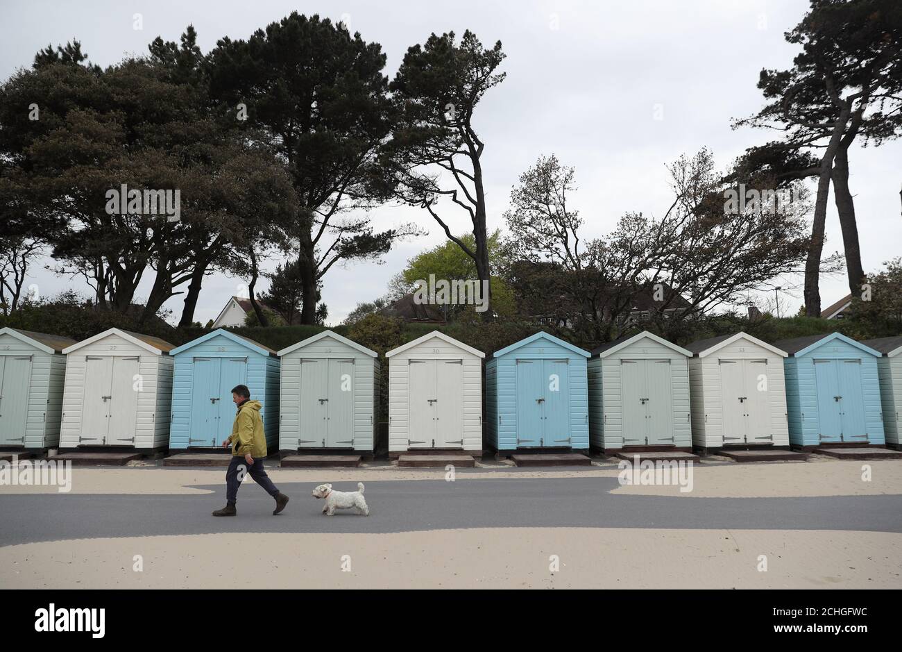 Eine Person geht mit ihrem Hund vorbei an Strandhütten Avon Beach in Christchurch, Dorset. Stockfoto