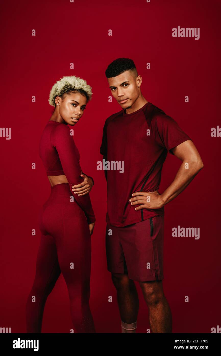 afroamerikanisches Sportpaar, das zusammen auf kastanienbraunem Hintergrund steht. Fitnesspaar in kastanienbrauner Fitness-Kleidung, die sich gegenüber steht. Stockfoto