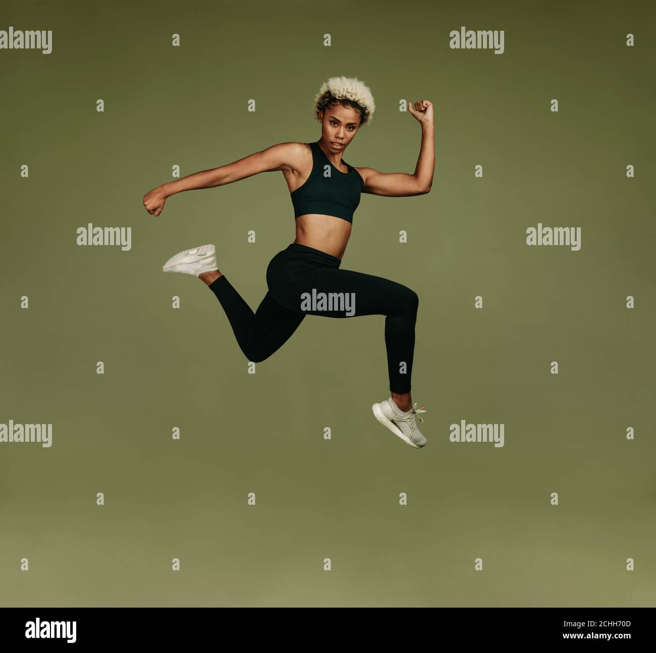 afroamerikanische Athletin macht Fitness-Übung. Frau tut Strecken in der Luft auf grünem Hintergrund. Stockfoto