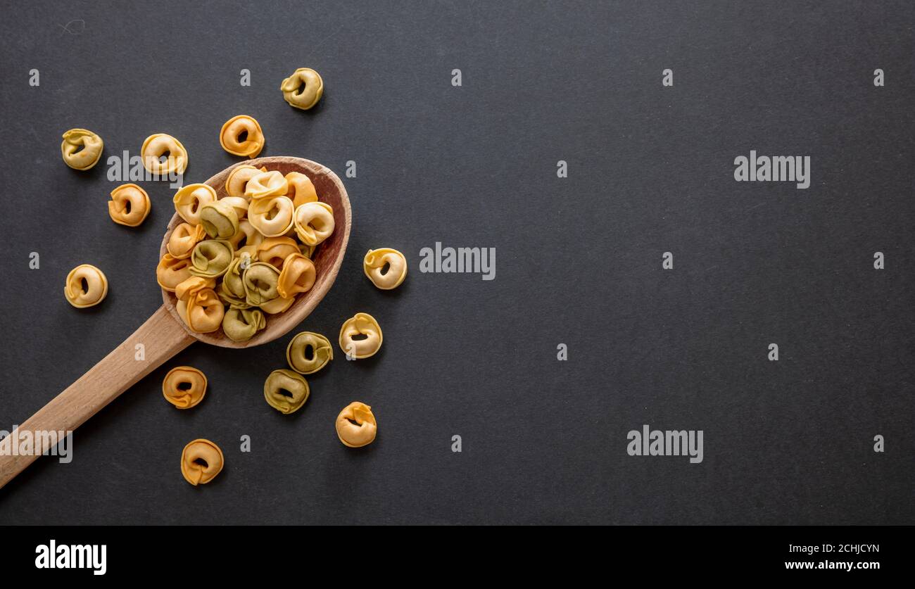 Pasta-Kochkonzept. Frische hausgemachte Tortellini auf einem Holzlöffel, schwarzer Stein Hintergrund, Draufsicht, Kopierraum Stockfoto