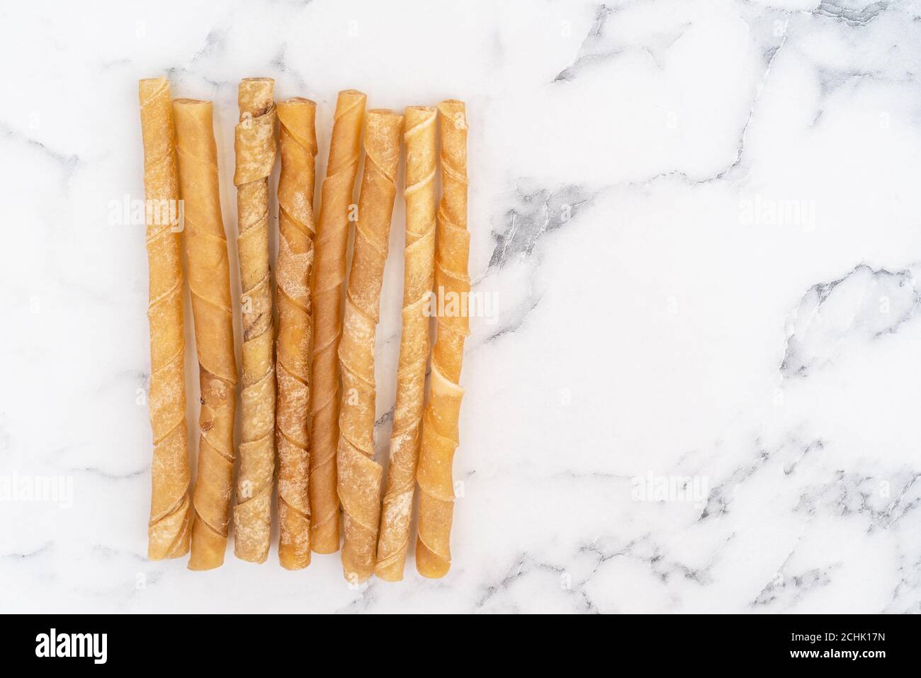 Rawhide Hund kaut vor einem weißen Marmor Hintergrund. Stockfoto