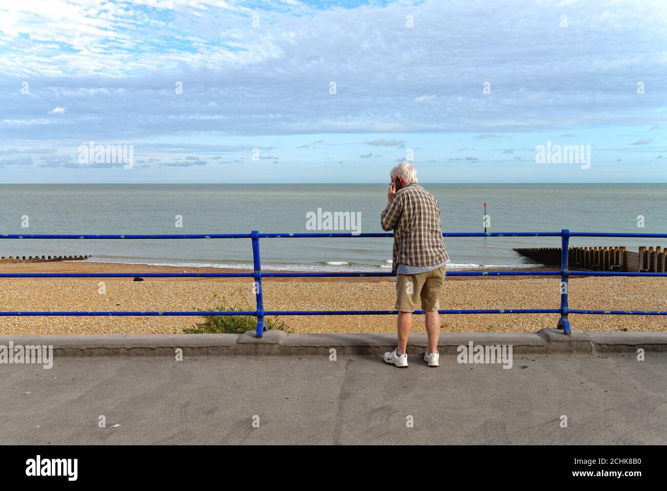 Eine Rückansicht eines älteren Herrn, der ein Mobiltelefon an der Küste von Eastbourne mit dem Meer im Hintergrund benutzt, East Sussex England Stockfoto