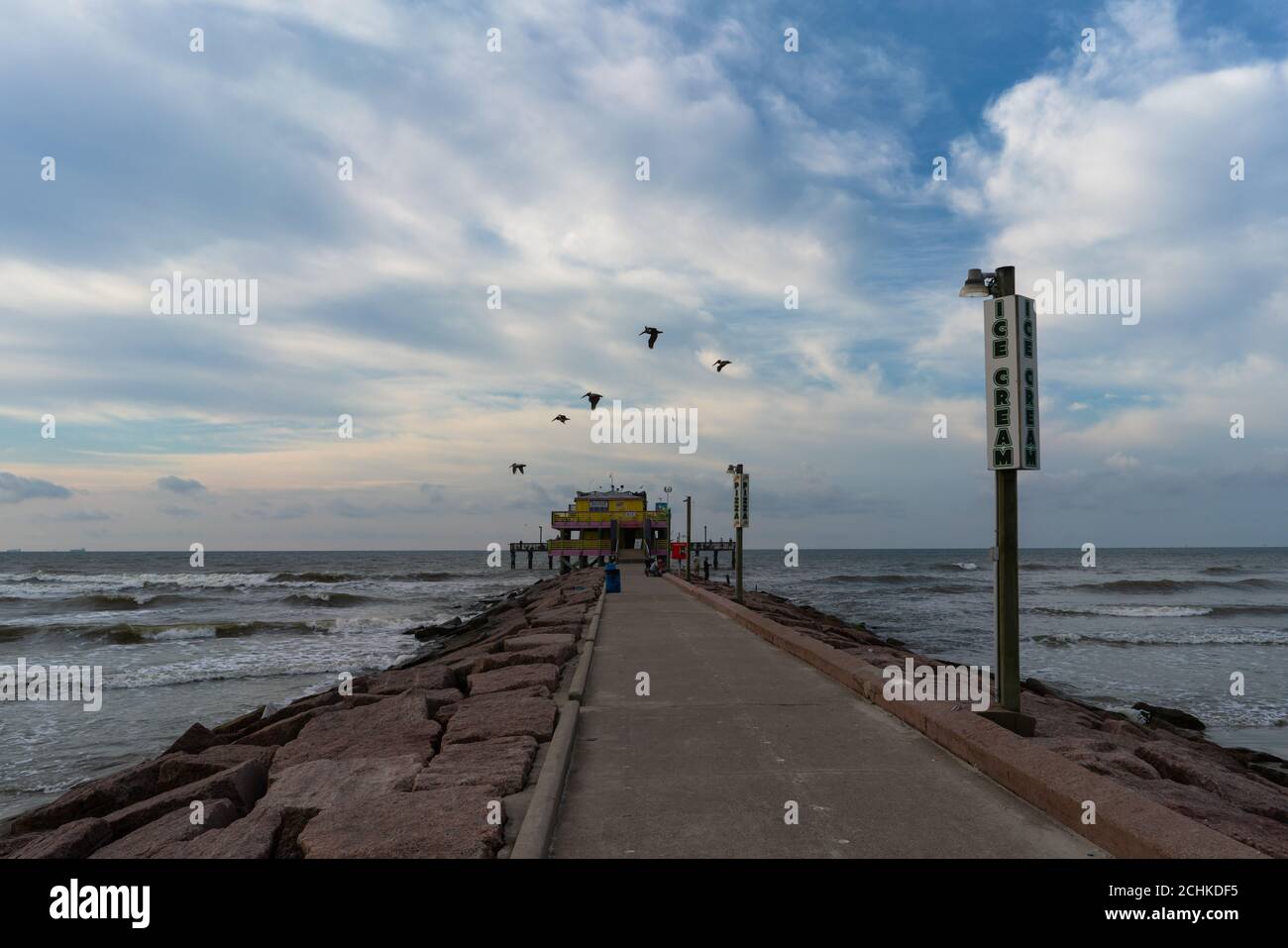 Vogelschar, der am frühen Morgen über einen Strandpier fliegt Stockfoto