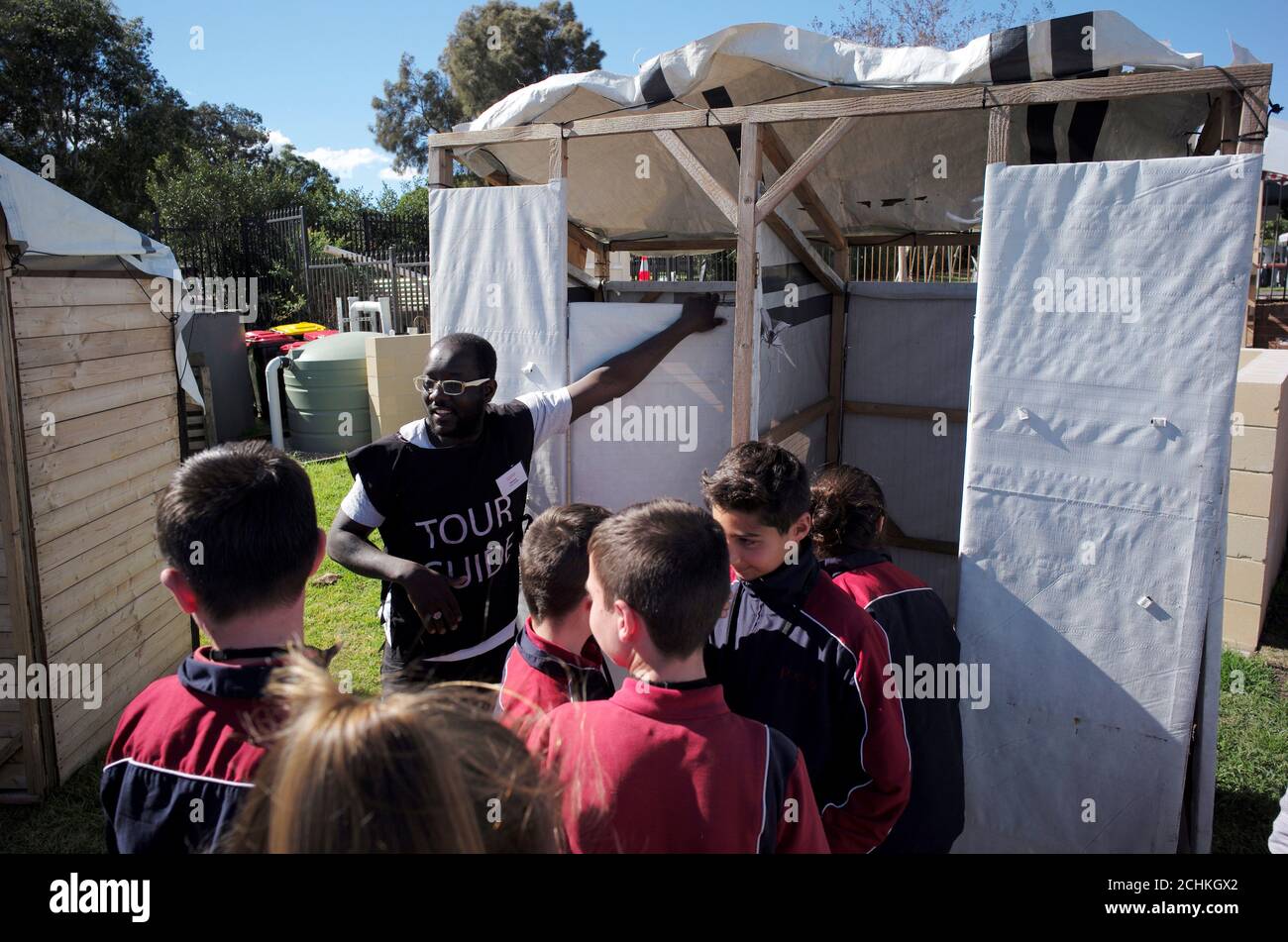 Khalid Abubaker aus Libyen, 33, zeigt Studenten einer Schule in Sydney eine Scheindusche für Flüchtlingslager in der Installation "Flüchtlingslager in meiner Nachbarschaft" in einem Sydney Park in Australien, 7. August 2017. Das temporäre "Flüchtlingslager"-Projekt, das von einem lokalen Sydney council gegründet wurde, wurde gegründet, um die realen Lebensbedingungen von Flüchtlingslagern auf der ganzen Welt zu replizieren und beschäftigt ehemalige Flüchtlinge als Reiseführer, um Australier über die Notlage von Millionen Vertriebenen in humanitären Notlagen weltweit zu informieren. REUTERS/Jason Reed Stockfoto